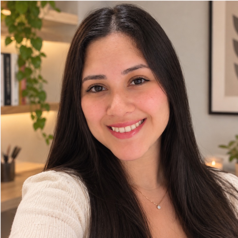 Retrato de Paola Jimenez sorrindo, de blusa clara, em um ambiente acolhedor